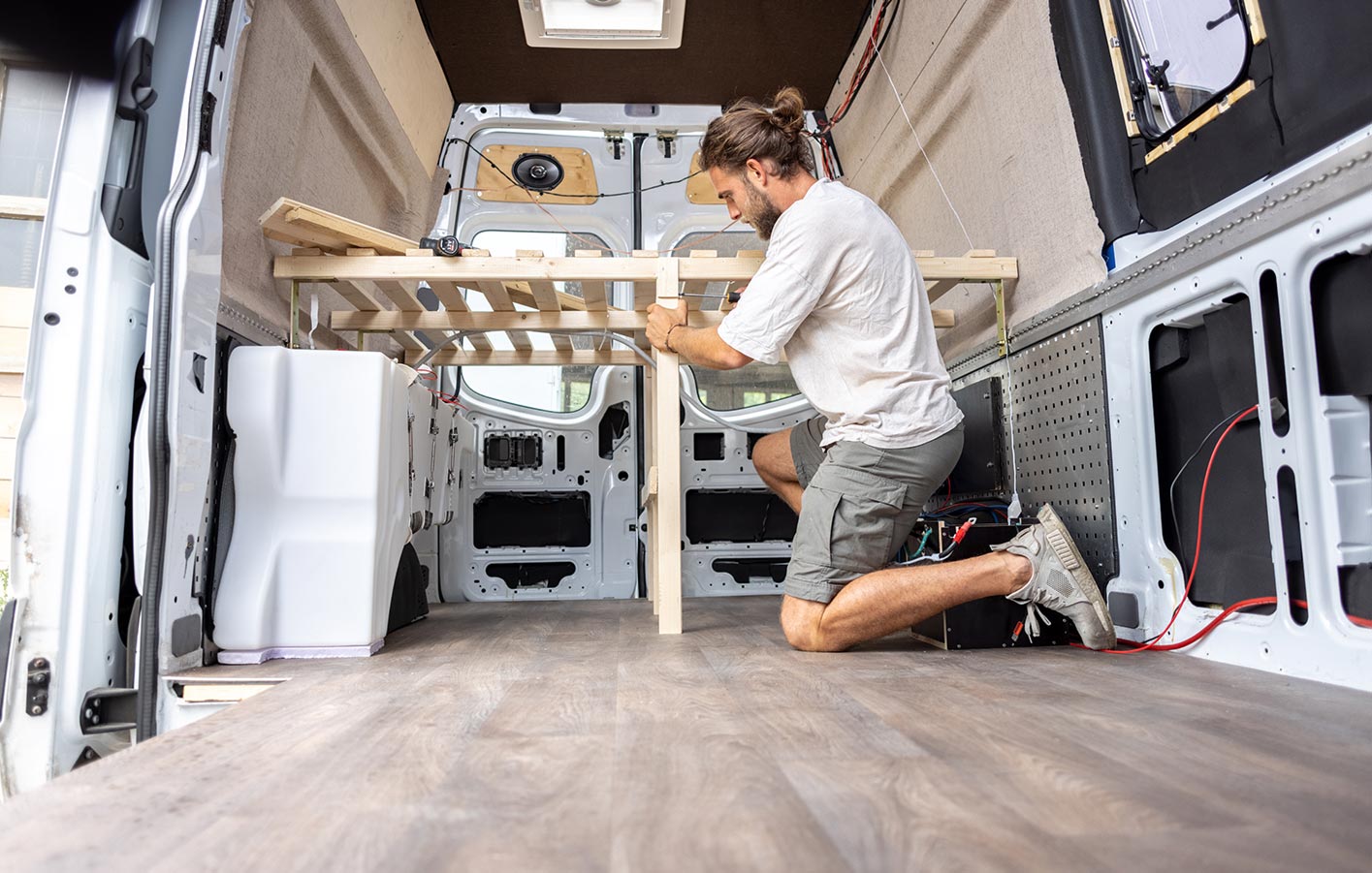 Ein Mann baut ein Bettuntergestell in einem Wohnmobil aus nachhaltigen Holzmaterialien, zeigt den praktischen DIY-Ausbauprozess.